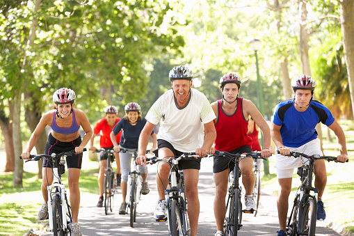 Group Of Cyclists On Cycle Ride Through Park During Summer