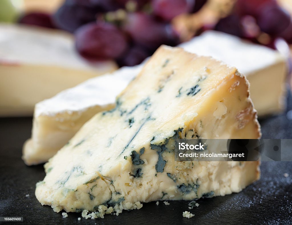 Ripe Stilton on cheeseboard A selection of cheeses and grapes arranged on a slate cheese board. Blue Cheese Stock Photo