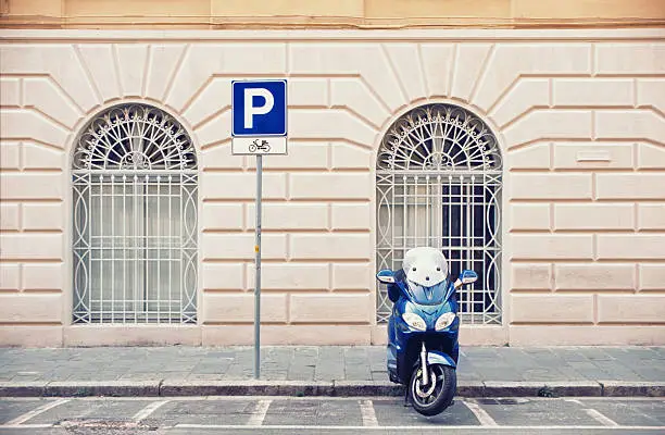 Iconic Italian scooter in a parking space designated for motorbikes. Pisa, Tuscany, Italy. Focus on the scooter. Slight toning applied.
