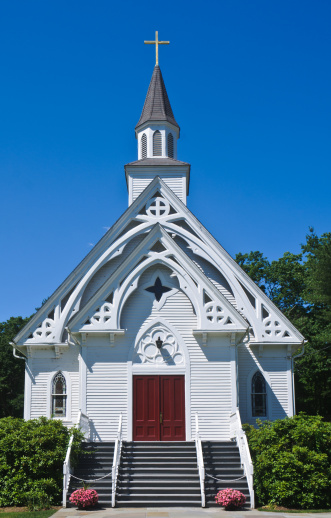 A beautiful white church with a rusty roof surrounded by dry trees under a cloudy sky