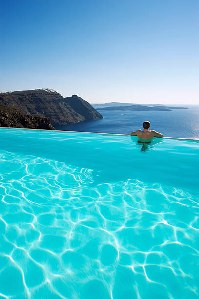 Santorini Greece Oia, young men in swim short relaxing in the pool looking out over the caldera of Santorini Island greece, infinity pool , young guy on luxury vacation in EuropeGreece. High quality photo