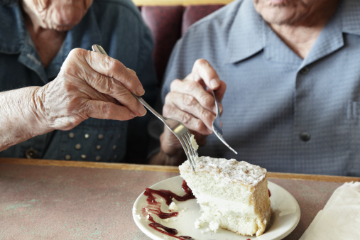 Grandma and Grandpa (who isn't thrilled at sharing what started out as HIS dessert!) are eating a large piece of cake. Slight motion blur on Grandma's hand and fork as she dives in from the left. Partially desaturated image.