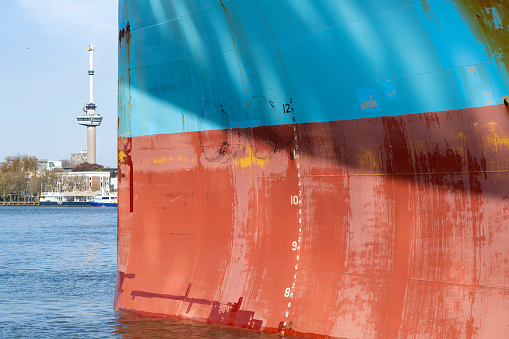 Close up view of the red and blue colored bow a ship with anchor hole, Load line mark and with patchy paintwork with in background the Maas river in Rotterdam, the Netherlands
