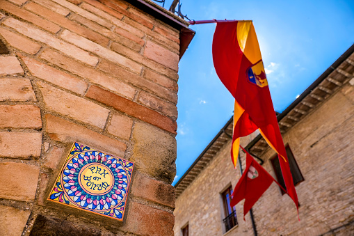 The Franciscan latin lemma Pax et Bonum (Peace and Good) along a stone alley in the medieval heart of Assisi in Umbria, central Italy. In addition to converting into the traditional greeting of peace among the faithful of St. Francis, 'Peace and Good' is also a lemma displayed on many houses in Assisi and not only as a sign of welcome and peace for all. Also in the photo, some flags with the emblems of the district, according to historical and medieval tradition. Famous for being the homeland of St. Francis and St. Clare, over the centuries Assisi and the spirituality of its sacred places have become a symbol of peace, a point of reference for tolerance and solidarity between peoples and between the different confessions of the world. The Umbria region, considered the green lung of Italy for its wooded mountains, is characterized by a perfect integration between nature and the presence of man, in a context of environmental sustainability and healthy life. In addition to its immense artistic and historical heritage, Umbria is famous for its food and wine production and for the high quality of the olive oil produced in these lands. Since 2000, the Basilica and the other Franciscan places in Assisi have been declared a World Heritage Site by UNESCO. Wide angle image in high definition quality.