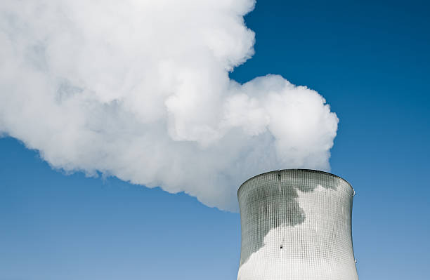 Nuclear Power Station Nuclear Power Station with steaming tower over clear blue sky. nuclear reactor stock pictures, royalty-free photos & images