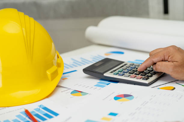 istock Asian engineer with architectural house plan project blueprint, graph and yellow helmet and engineering construction tools. 1556073214