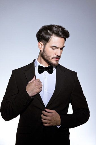 Studio portrait of a young caucasian man in a tuxedo, looking to the side, against plain studio background