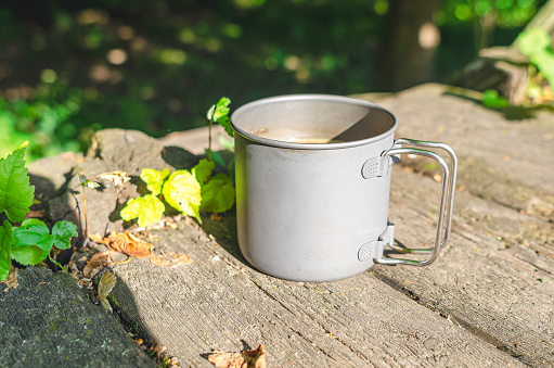 Metal cup on a wooden table in nature. Tea in nature