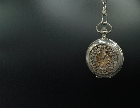 Silver metal pocket mechanical watch hanging on a black background
