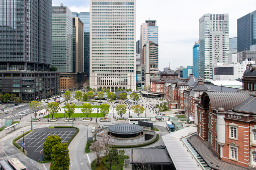 Tokyo, Japan-April 2023; High angle view over the Marunouchi Ekimae square, granite-paved with lawns and surrounding skyscrapers bordering the red-brick Tokyo Station