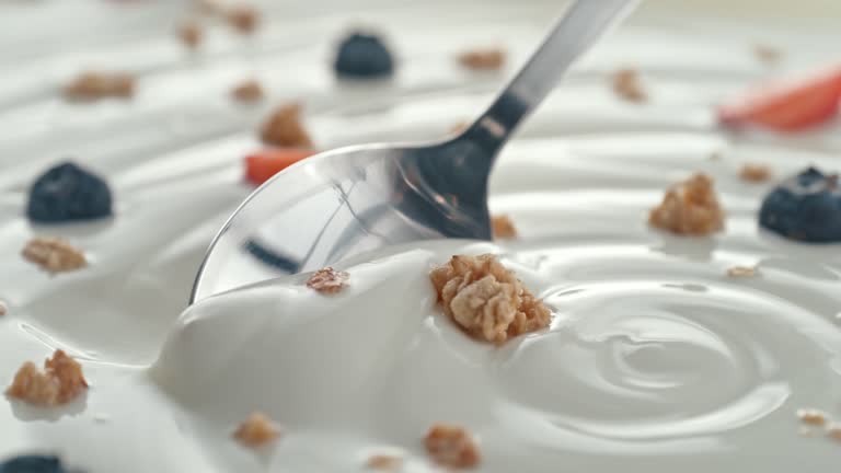 Granola with Blueberries and Strawberries Scooped with Silver Spoon from Creamy Yogurt in Macro and Slow Motion