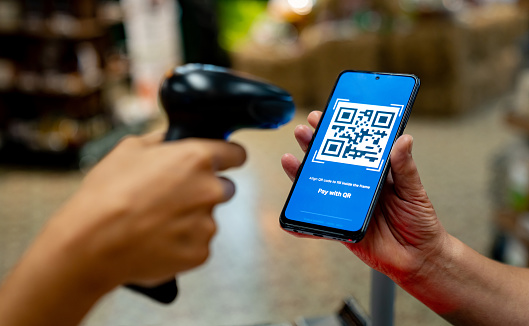 Cashier scanning a QR code to make a payment at the supermarket - small business concepts