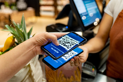 Close-up on a woman at the supermarket scanning a QR code with her cell phone to make a mobile payment