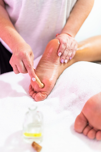 Young woman having her feet scrubbed in beauty salon. Close up of hands of young masseur washing feet of woman in spa in grey bowl with water and pink petals. Girl getting spa massage treatment in luxury beauty salon: foot reflexology and chiropody therapy.