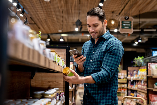 Man shopping at the supermarket and scanning a label with his cell phone