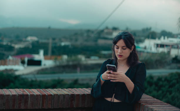 istock young woman, sending a text message with her smart phone, from a balcony, with a green background of vegetation, copy space 1556205312