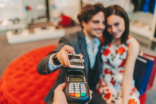 Young couple making contactless payment with smartphone in the mall