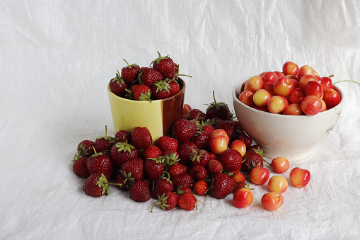 A mug with strawberries and a cup with cherries on a white background.