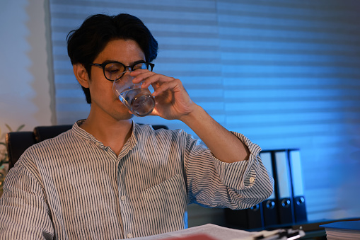 Young businessman drink water to refresh himself during work overnight