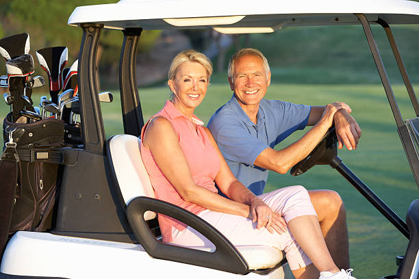 senior casal dirigindo em buggy de golfe - golf course golf people sitting imagens e fotografias de stock