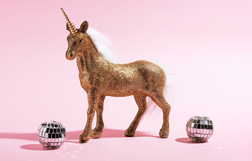 Golden shiny unicorn toy and disco balls on pink background. Holiday card idea.