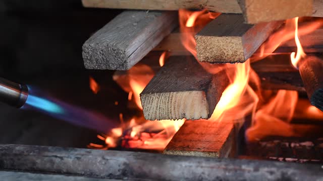 Ignite firewood in a fireplace with a gas burner.