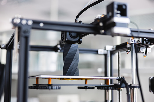 Frontal view of a 3D printer in action creating a 3D object at a laboratory. The background of the photo is defocused.