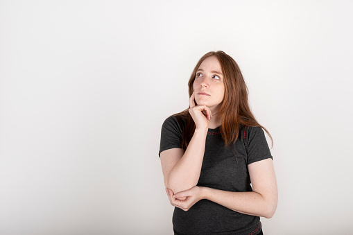 Portrait of a young red haired woman on a white background, with a thoughtful expression, making a decision