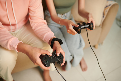Hands of teenage girls playing videogame at home to relax after classes