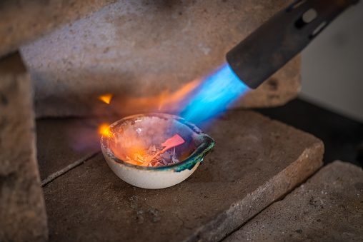 a craftsman jeweler with a blowtorch melts silver or gold in a small furnace in a jewelry workshop.