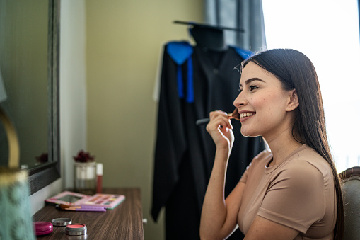 Young woman applying make-up for graduation day at home