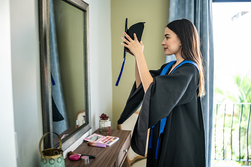 Young woman graduate getting ready looking at mirror at home