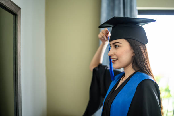 istock Young woman graduate getting ready looking at mirror at home 1556527019