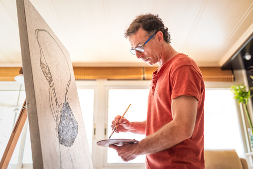 Man is an artist, holding a brush and drawing an abstract picture at his home