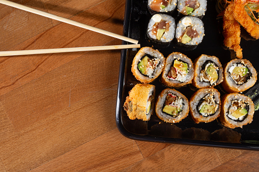 Sushi mix on black plate and dark dish isolated on slate background.