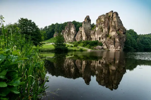 Scenic view of the Externsteine stones over the calm water of the nearby pond, Teutoburg Forest, Germany