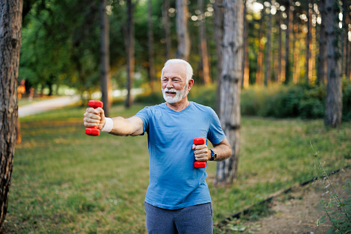 Senior man exercising with weights in nature