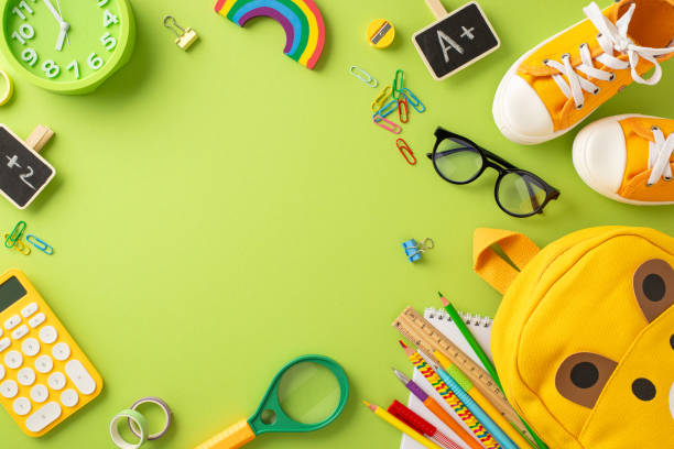 istock Get ready for first day of elementary school. Top view of playful bear-shaped bag, crayons, drawing pad, A+ achievement symbol, sneakers and more on soft green surface with blank frame for text or ad 1556577693