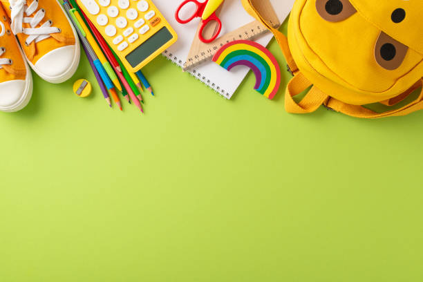 istock Attract attention from parents and educators with top-down image of yellow child backpack overflowing with array of colorful school supplies. Perfect for educational campaigns on light green backdrop 1556578201