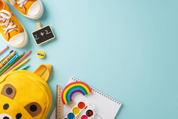 istock Growing curious minds. Top view of a cute children's backpack filled with lively school essentials and shoes to walk on a pastel blue backdrop, perfect for text or promotional content 1556578468