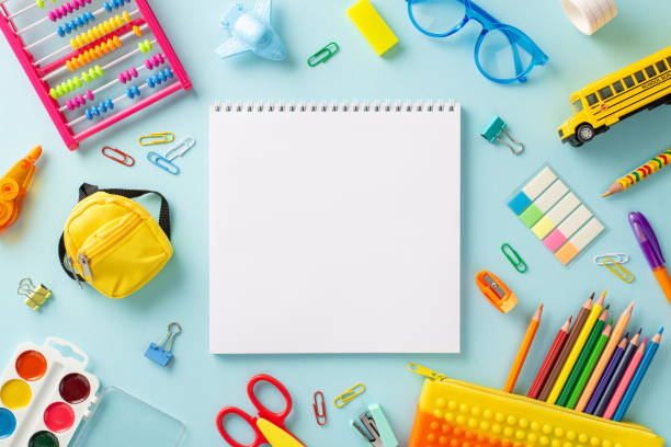 istock Education for small kids concept. Creative top view photo of empty notepad page offering copy-space, glasses, pencil case and other colorful school supplies on isolated pastel blue background 1556580769