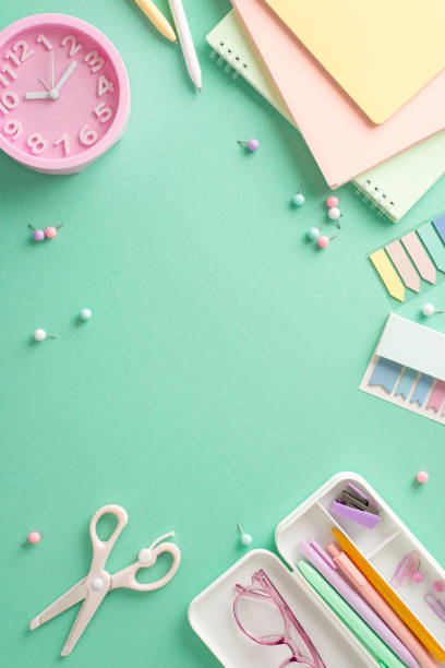 istock Ready for productivity concept. Vertical top view of efficient workspace tools, notebooks, pens, sticky notes, pushpins, scissors, clock, glasses, on teal background with empty frame for text or ad 1556580771