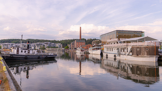 Lahti, Finland. June 17th, 2023. The lake Vesijärvi in the summet evening in shades of blue and vessels anchored in the port. Old factory and Sibelius concert hall in the background.