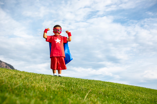 Young boy dressed as a superhero standing on grass. He is ready to protect the world from mayhem. Utah, USA.