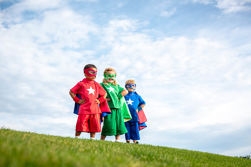 Two boys and a girl dressed as superheroes in masks and capes are ready to save the planet from peril. Utah, USA.