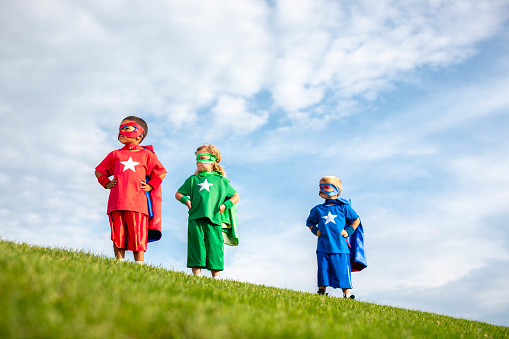 Two boys and a girl dressed as superheroes in masks and capes are ready to save the planet from peril. Utah, USA.