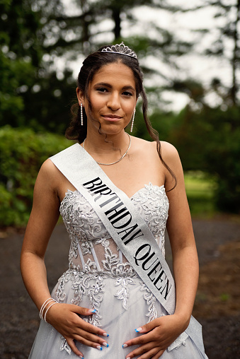 Portrait of beautiful hispanic teenager posing for Quinceanera. She is dressed with beautiful party gown, honouring her cubans origins and traditions. She has long brown hair and braces. Vertical waist up indoors shot with copy space. This was taken in Quebec, Canada.