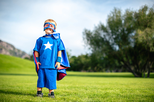 Young boy dressed as a superhero standing on grass. He is ready to protect the world from mayhem. Utah, USA.
