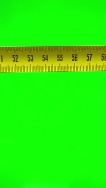 Top View Close Up Of Man's Hands With Measuring Ruler On green Background. Female hands in the frame on a green chromakey background are measured with a yellow centimeter