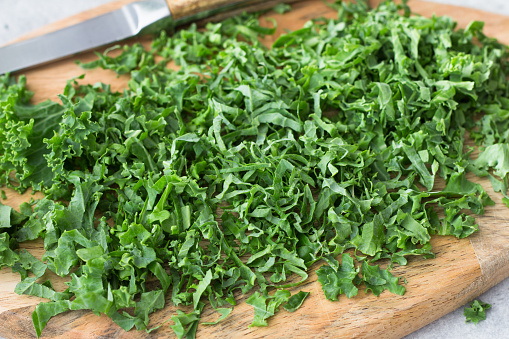 Wooden board of sliced curly kale, close-up, selective focus. Cooking a delicious healthy meal.